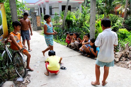 Các em nhỏ chơi đùa dưới vườn dừa mát rượi trước sân.