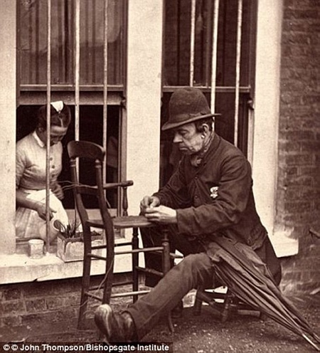 Một người đàn ông sửa đồ nội thất bên vệ đường. (ảnh: Bishopsgate Institute).