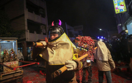 Một người tham gia lễ hội đội chiếc mũ bảo hiểm tinh nghịch, vác theo cả dây pháo tép mà không sợ chúng có thể nổ bất cứ lúc nào vì những tia lửa bay lạc.