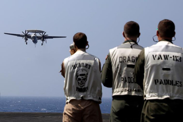 Nhân viên trên boong theo dõi chiếc phi cơ trinh sát E-2C Hawkeye hạ cánh.