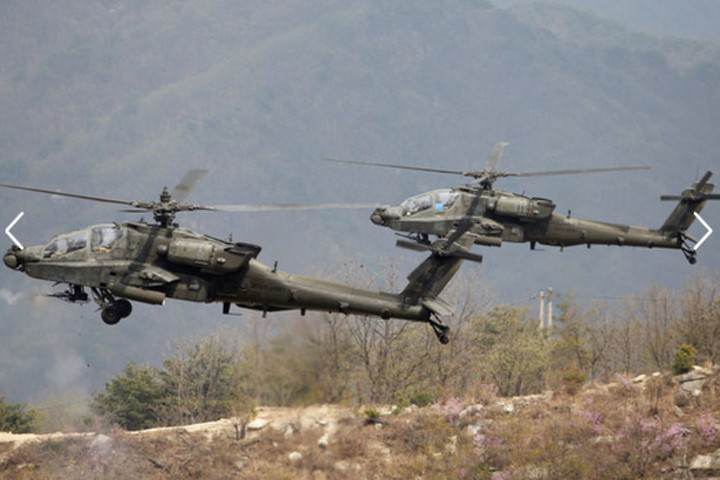 ​Trực thăng AH-64 Apache của lục quân Mỹ bay phía trên các xe thiết giáp. Ảnh: Reuters.