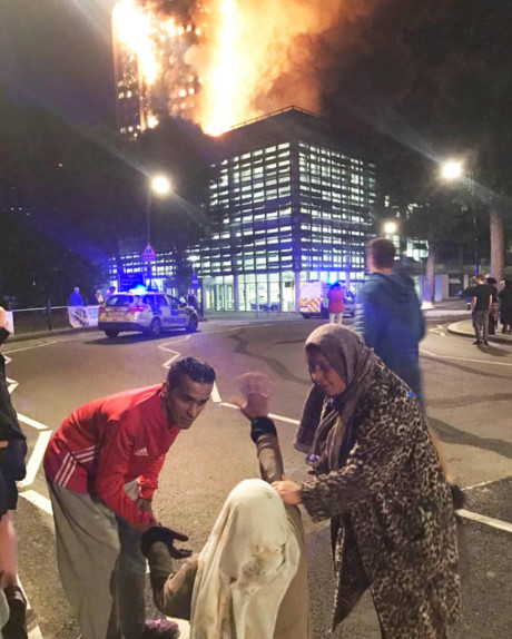 Một phụ nữ ra được ngoài và đau khổ nhìn tòa chung cư bốc cháy trong sự bất lực. Ảnh: Daily Mail.
