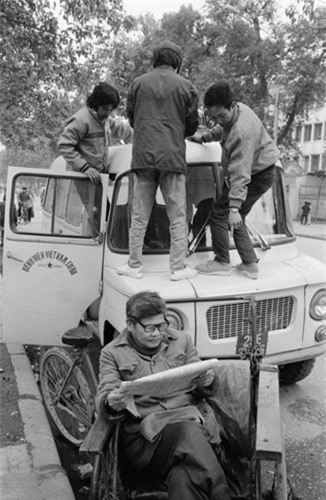 Người lái xích lô nhàn nhã đọc báo cạnh các nhân viên tất bật của Bệnh viện Việt Nam - Cuba, 2/3/1990. Ảnh: Magnumphotos.com