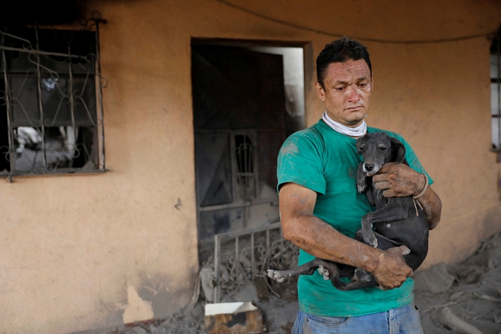 Ông Walter Amilcar Garcia (42 tuổi) ôm chú cún vừa may mắn được cứu sống của người em trai, đứng trước ngôi nhà đổ nát của mình tại ấp El Rodeo, Escuintla - Ảnh: REUTERS