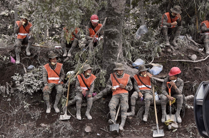 Những người lính cứu hộ nghỉ ngơi giữa cuộc tìm kiếm. Họ đã vật lộn với tro và nham thạch liên tục 3 ngày, kể từ sau khi ngọn núi Fuego phun trào - Ảnh: AFP