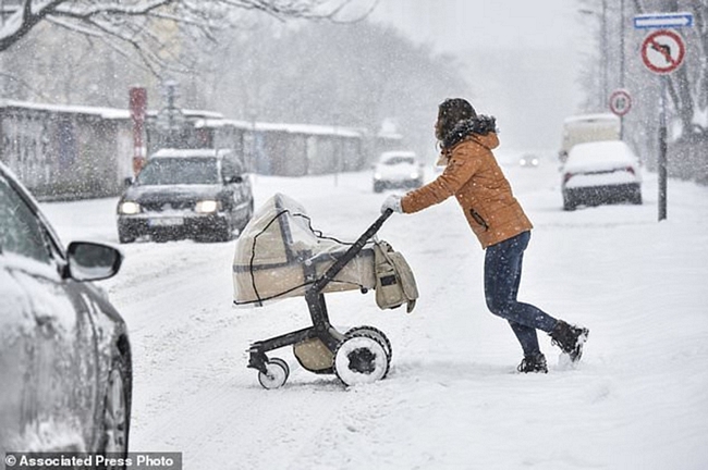 Một người phụ nữ đang đẩy chiếc xe nôi qua đường dưới trời tuyết rơi dày ở Bratislava, Slovakia. Ảnh: AP