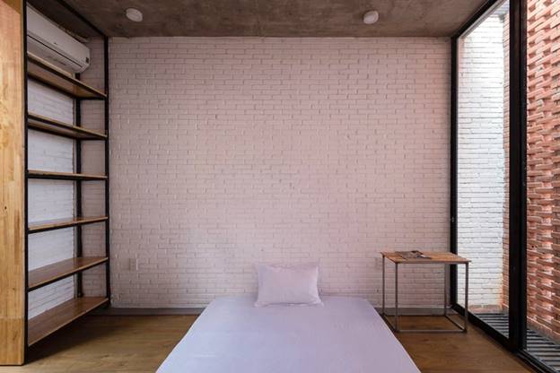 Phòng ngủ tầng 3 có một lớp gạch xây tạo lỗ rỗng bên ngoài. Để tăng hệ số chiếu sáng, bức tường đầu giường được sơn trắng.