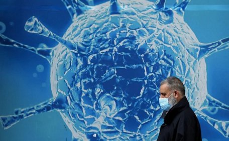  Một người đàn ông đeo khẩu trang đi qua hình minh họa virus SARS-CoV-2 bên ngoài một trung tâm nghiên cứu khoa học ở Anh. Ảnh: Reuters
